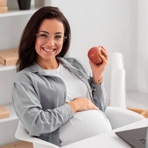 Smiling pregnant woman at home holding an apple, Dr. Deepali Mittal, gynecologist in Indore